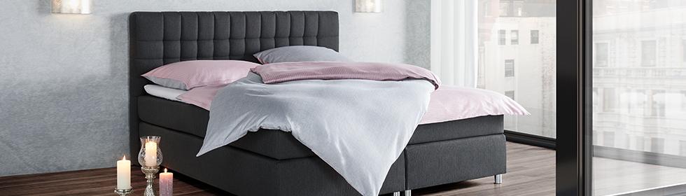 Dreiteiliger Boxspringbett-Aufbau: Boxspringbett mit Stoffüberzug in Anthrazit und Bettzeug in rosa und grau von mömax.