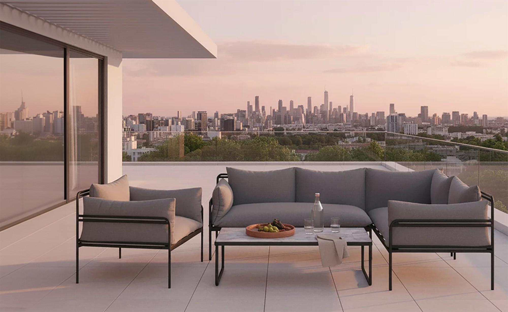 Modern kültéri bútor szett szürke párnákkal és fekete fém vázzal egy panorámás tetőteraszon, városi kilátással.