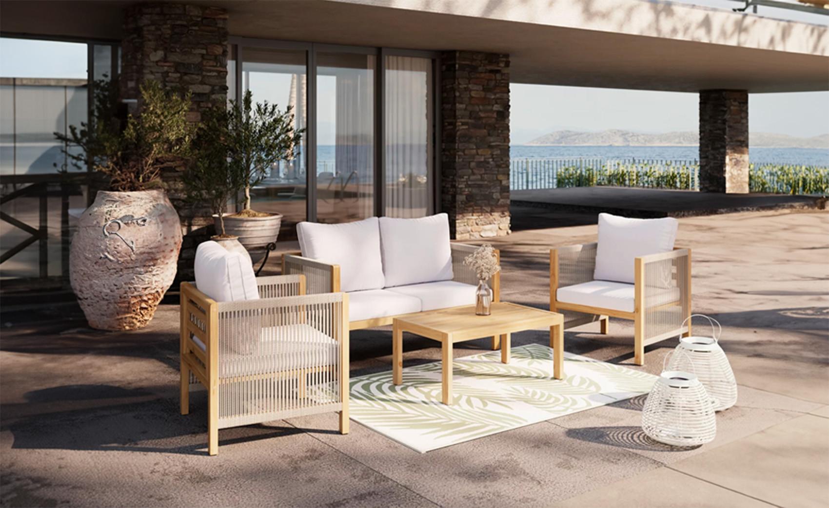 Modern kerti bútor szett világos fa vázzal és fehér párnákkal egy tengerre néző teraszon, kávézóasztallal, kültéri szőnyeggel és dekor lámpásokkal.