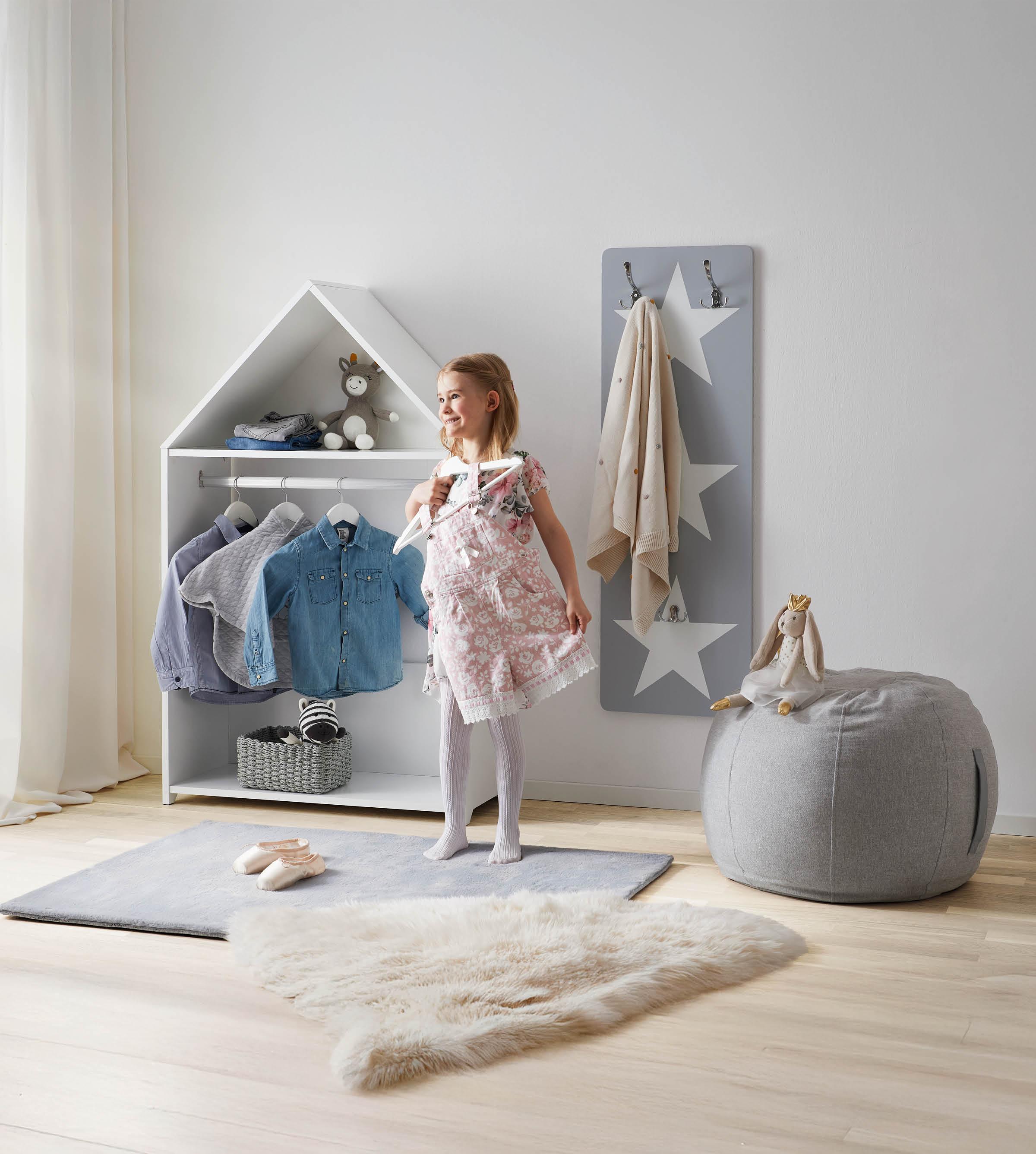 Kind mit Kinderkleiderschrank und Kindergarderobe im Hintergrund