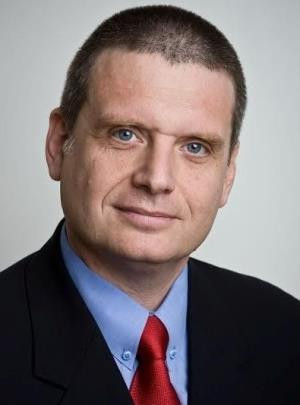 Simonyi András ügyvezető igazgató üzleti fotója amin fekete öltönyt visel kék inggel és piros nyakkendővel.