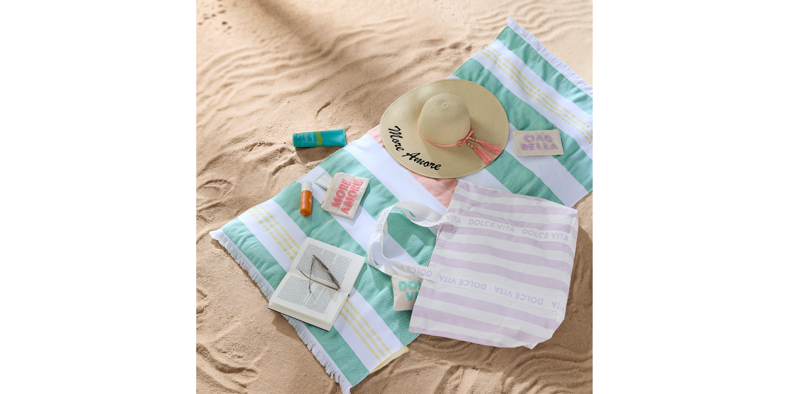 Bunt gestreiftes Strandtuch auf Sand mit Strandhut und Accessoires