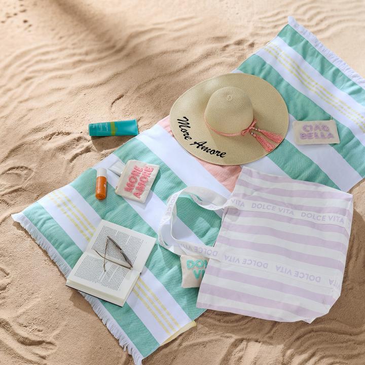 Bunt gestreiftes Strandtuch auf Sand mit Strandhut und Accessoires