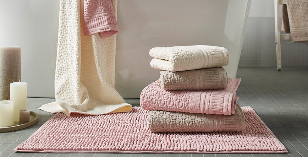 Gestapelte Handtücher in Beige, Rosa und Weiß, auf einer rosafarbenen Badematte, von mömax.