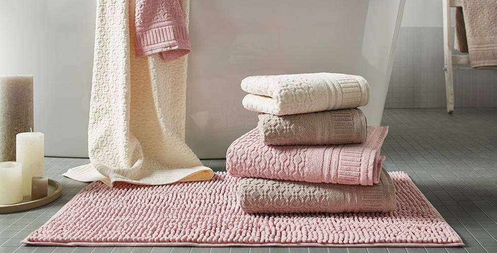 Gestapelte Handtücher in Beige, Rosa und Weiß, auf einer rosafarbenen Badematte, von mömax.