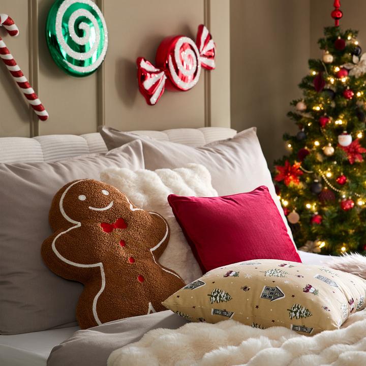 Bett mit rotem Kissen und Kissen in Lebkuchenform, Christbaum im Hintergrund