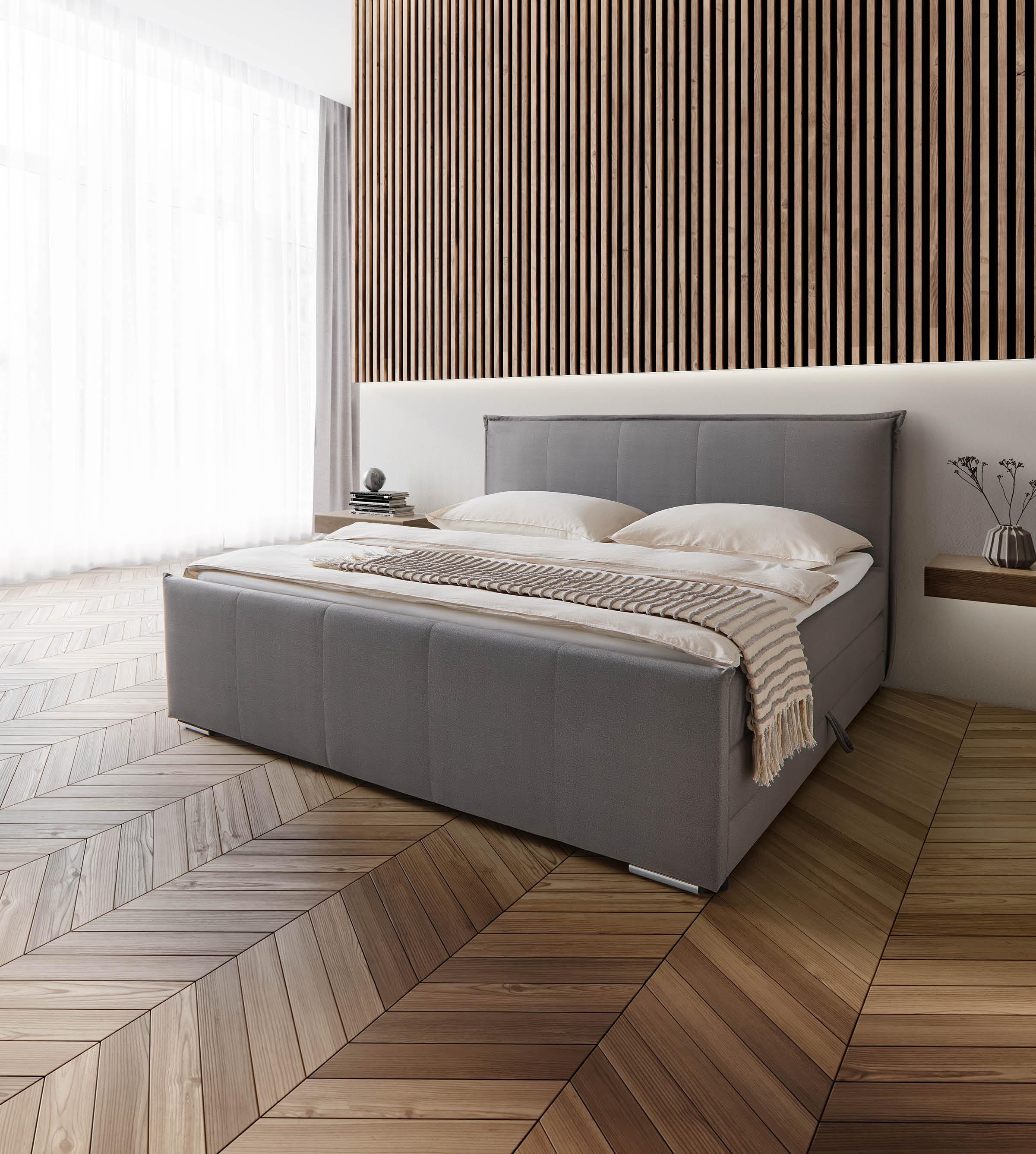 Graues Boxspringbett auf dunklem Holzboden und vor Holzwand