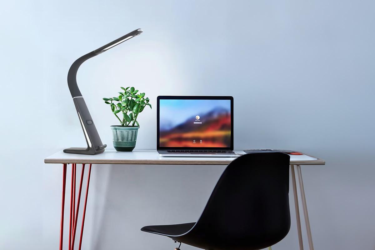Minimalista íróasztal laptoppal, modern asztali lámpával és kis szobanövénnyel, előtte fekete székkel.