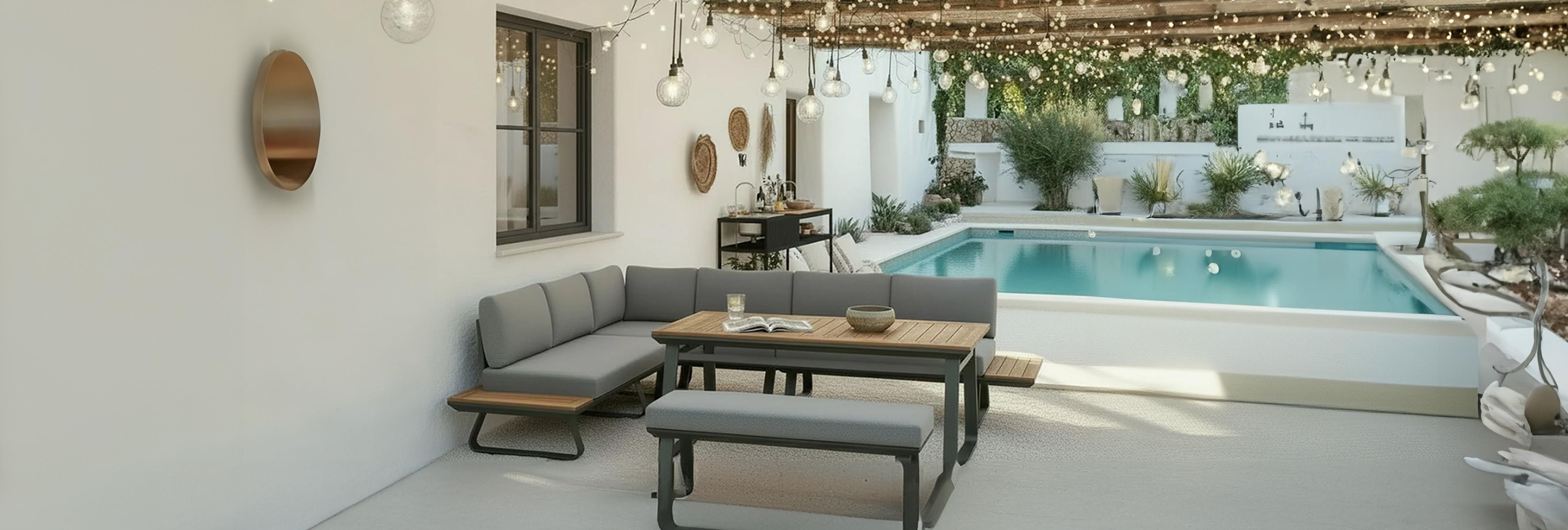 Modern kültéri lounge sarokkanapé és fa asztal egy hangulatfényekkel díszített, fedett teraszon a medence mellett.