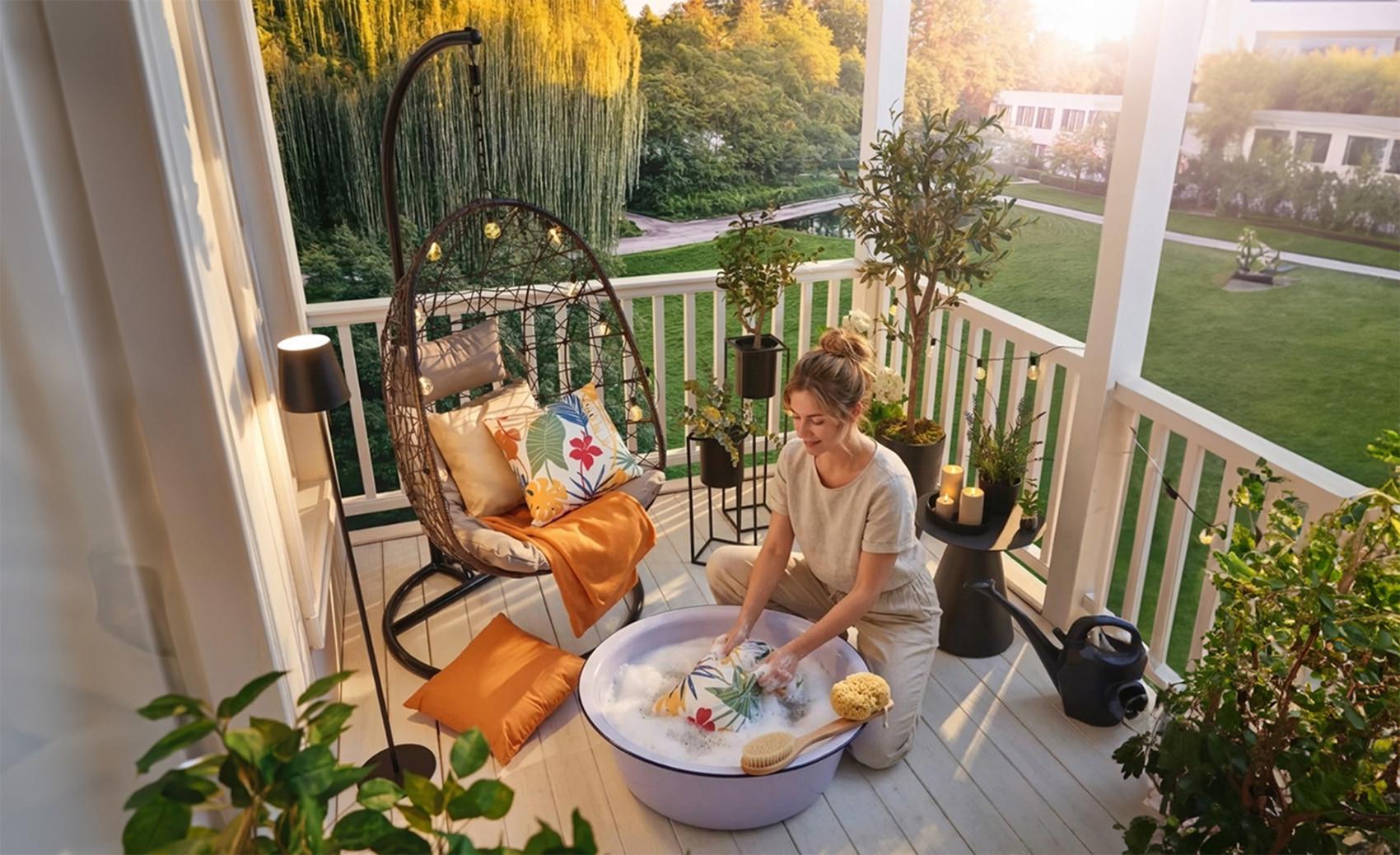 20-as éveiben járó nő meleg, szappanos vizes lavórban kézzel mossa a kerti párnahuzatot a napfényes teraszon, szivaccsal és puha kefével a kíméletes tisztításért.