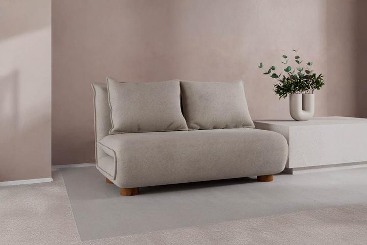 Beiges Schlafsofa mit weißem Couchtisch daneben vor rosa Wand