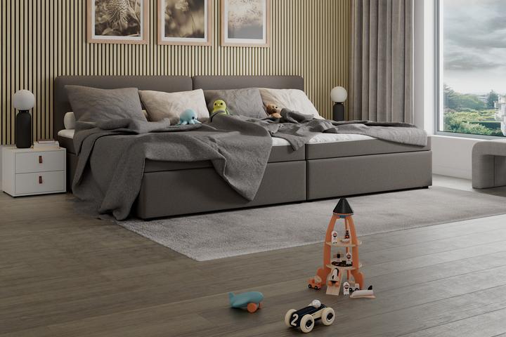 Zwei graue Betten, heller Teppich, weißes Nachtkästchen, Tischleuchte